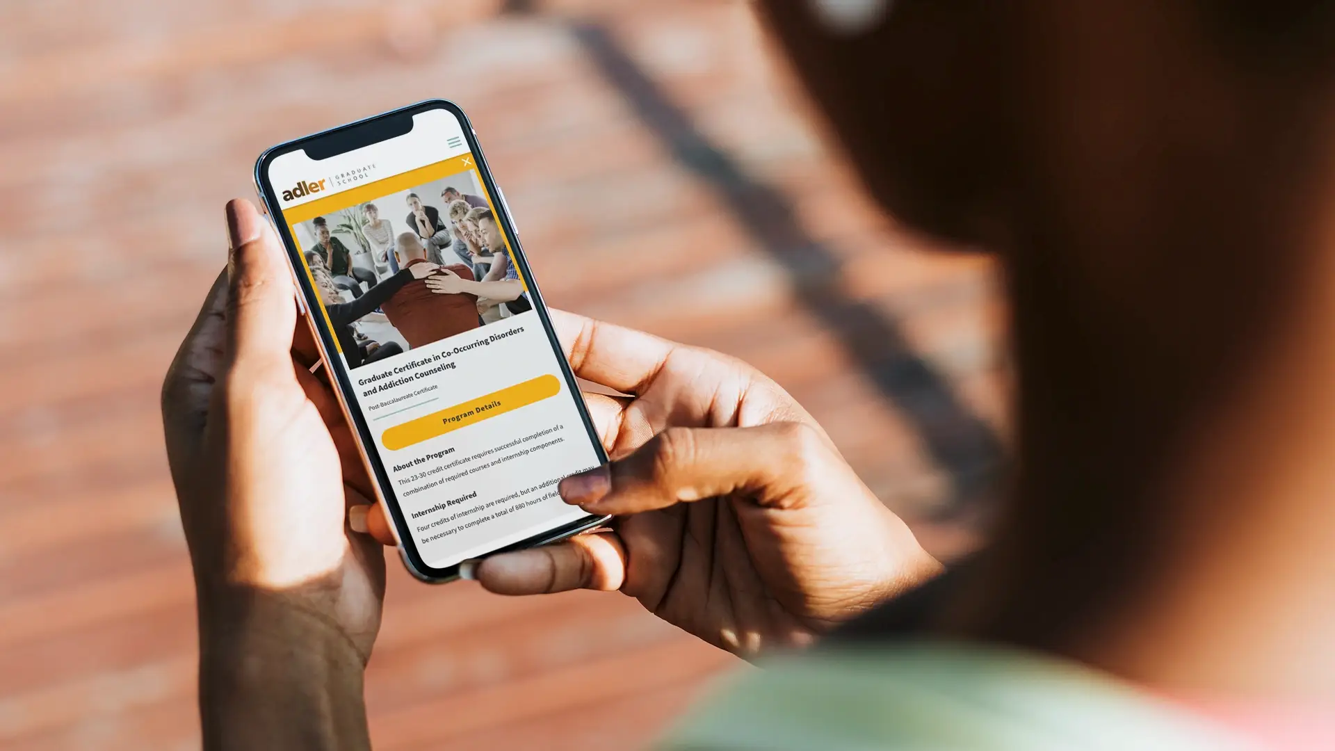 Closeup photo of a person using a mobile device with the new Adler Graduate School website displayed on the screen.